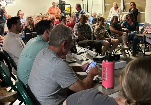 Community meeting with seated and standing attendees.